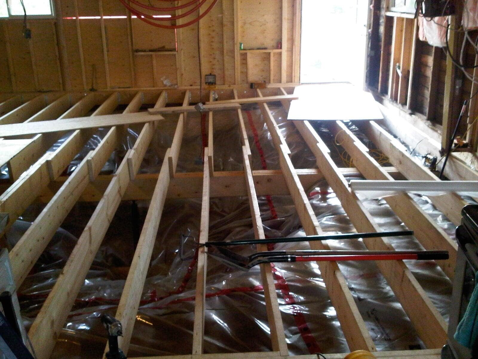 Floor joists installed over a dirt floor with poly vapour barrier during a grain bin conversion project